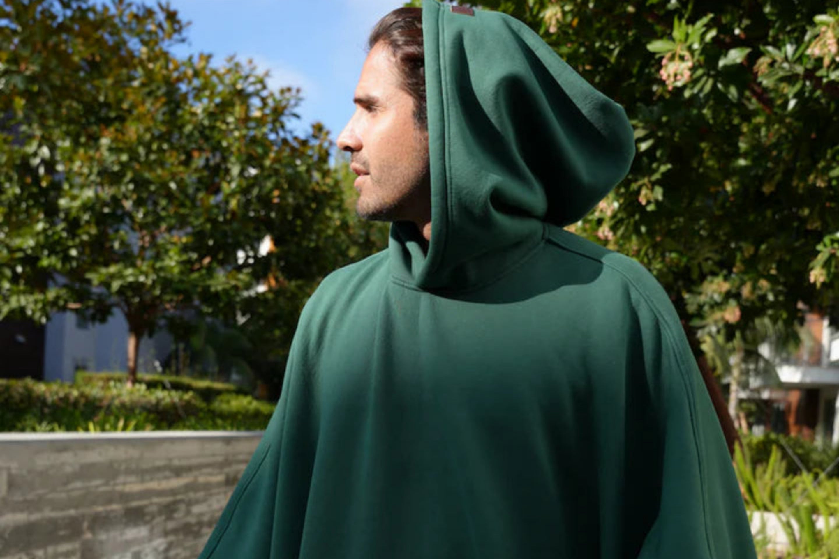 Person wearing a green hooded cloak standing outdoors with trees in the background